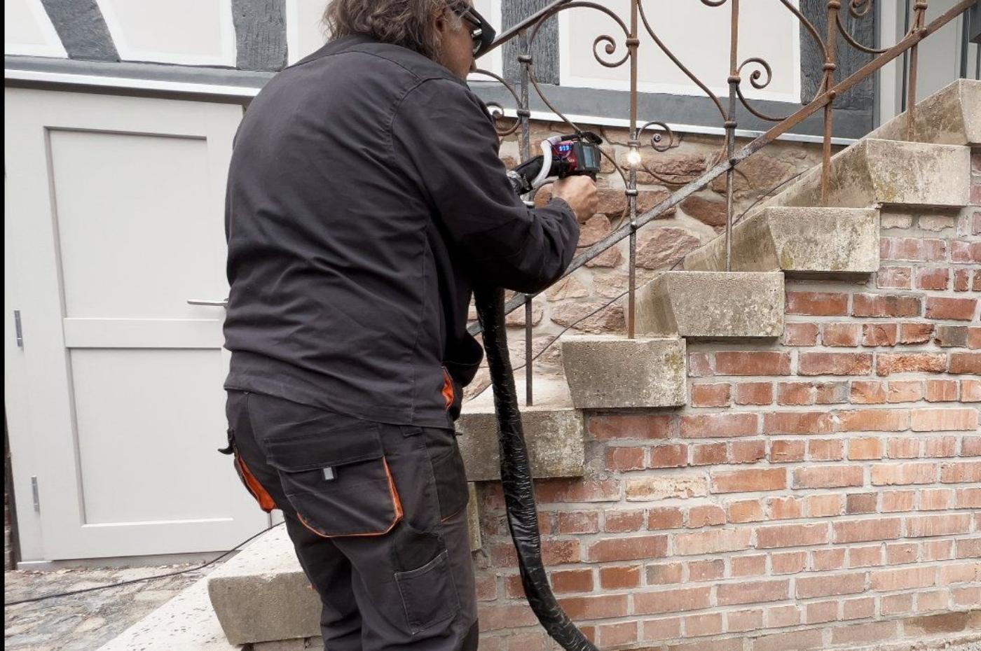 Mitarbeiter des L & L Hausmeisterservice reinigt in Wetter (Hessen) die Sandsteinstufen und das Mauerwerk eines Fachwerkhauses.